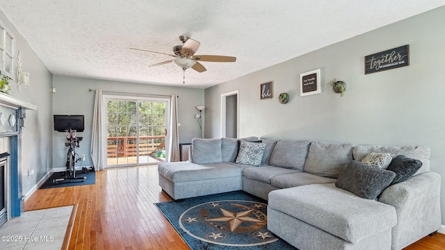 living area with ceiling fan, a textured ceiling, baseboards, and hardwood / wood-style flooring