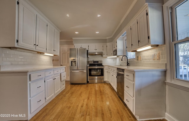 kitchen with stainless steel appliances, light countertops, white cabinetry, a sink, and under cabinet range hood