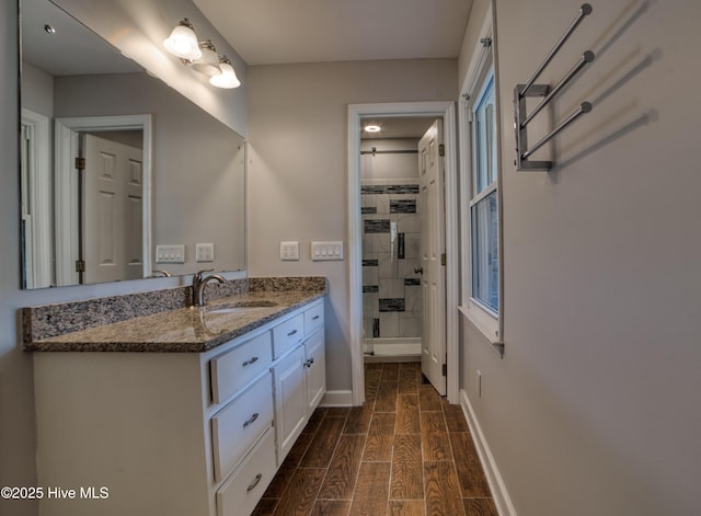 bathroom featuring wood finish floors, vanity, baseboards, and walk in shower