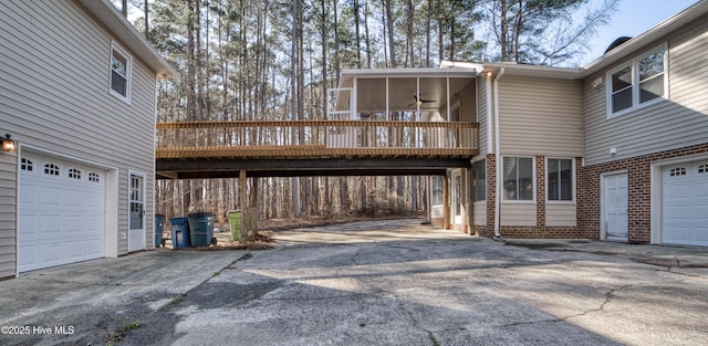 exterior space with brick siding, a ceiling fan, a garage, driveway, and a wooden deck