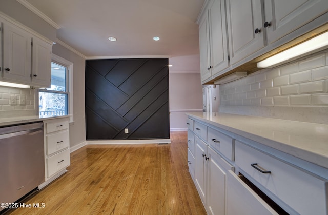 kitchen featuring ornamental molding, light countertops, light wood-style floors, white cabinetry, and stainless steel dishwasher