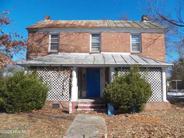 view of front of house featuring a standing seam roof, a chimney, and brick siding