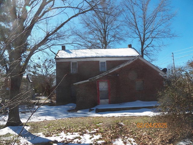 view of snow covered exterior featuring a chimney and brick siding