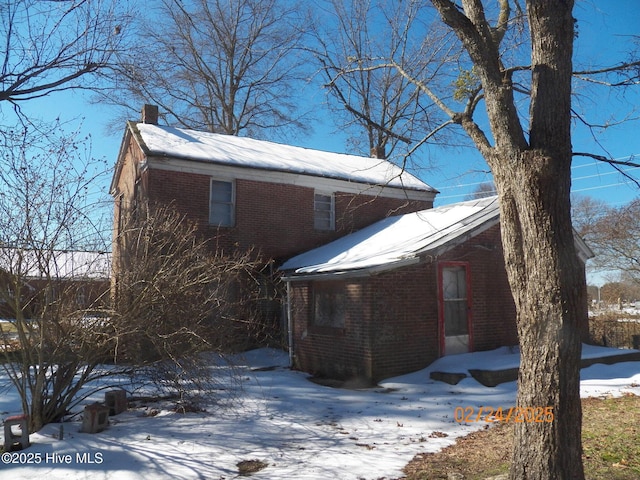 snow covered property with a chimney and brick siding