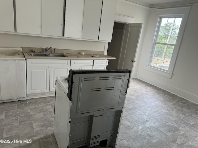 kitchen featuring baseboards, white cabinets, stone finish floor, light countertops, and a sink