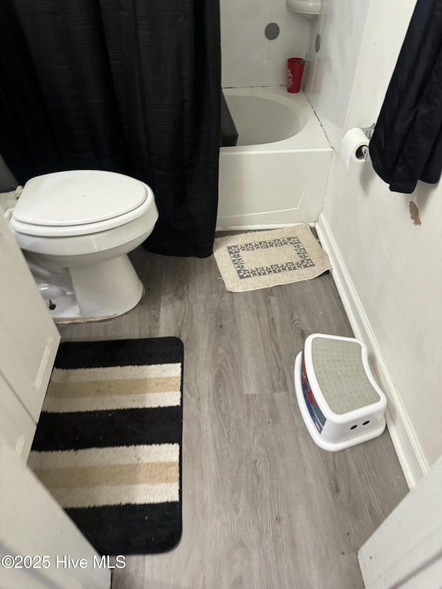 full bathroom featuring shower / tub combo, baseboards, toilet, and wood finished floors