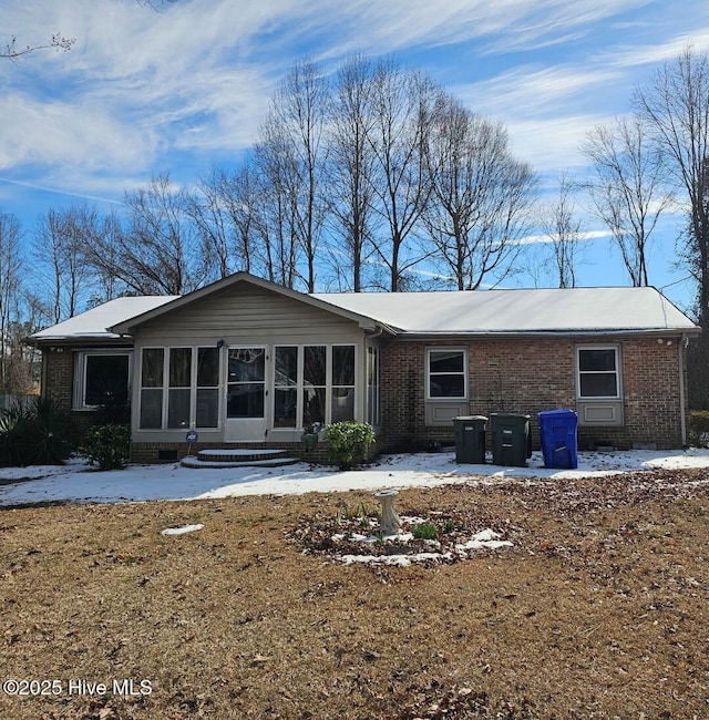 snow covered rear of property with a sunroom and brick siding