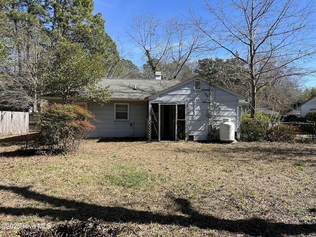 rear view of house featuring a yard, a chimney, and fence