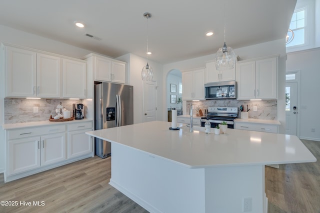 kitchen featuring arched walkways, appliances with stainless steel finishes, light wood finished floors, and white cabinetry