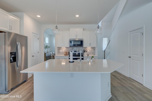 kitchen featuring arched walkways, light countertops, appliances with stainless steel finishes, light wood-type flooring, and decorative backsplash