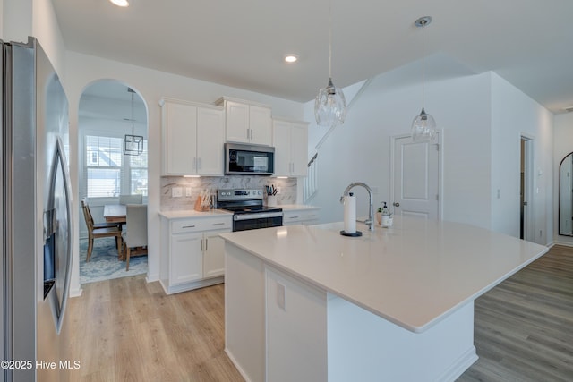 kitchen with light wood-style flooring, stainless steel appliances, a sink, white cabinetry, and decorative backsplash