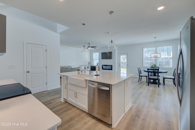 kitchen with light wood finished floors, stainless steel appliances, a large fireplace, white cabinets, and a sink