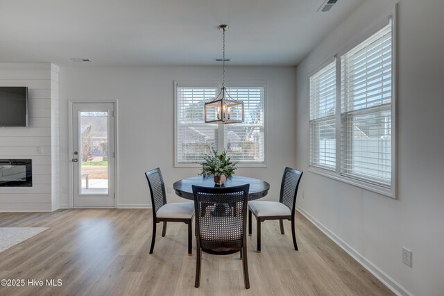 dining area featuring a large fireplace, light wood finished floors, visible vents, and baseboards