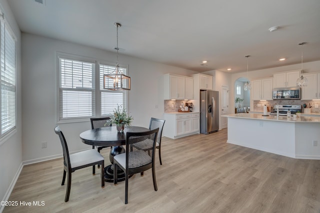 dining area featuring light wood-style floors, arched walkways, baseboards, and recessed lighting