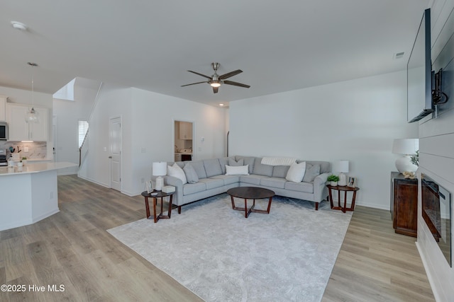 living room featuring light wood-type flooring, ceiling fan, a fireplace, and baseboards