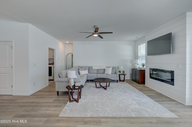 living room with ceiling fan, a fireplace, baseboards, and light wood-style floors