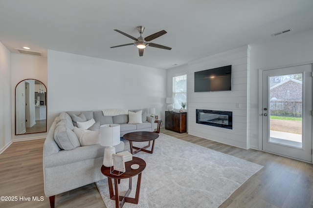 living room featuring ceiling fan, a fireplace, visible vents, and wood finished floors