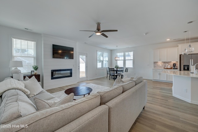 living area with light wood-style flooring, a large fireplace, a ceiling fan, visible vents, and baseboards