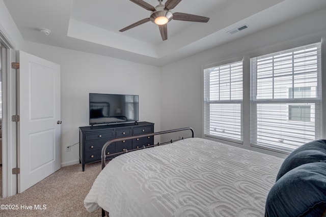 bedroom with light carpet, ceiling fan, a tray ceiling, and visible vents