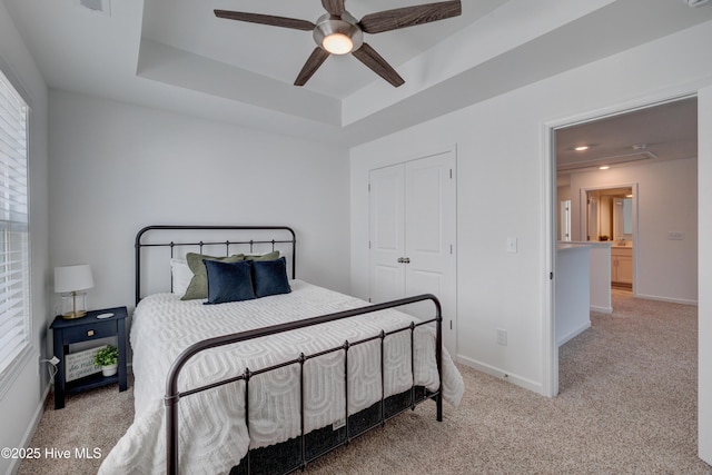 carpeted bedroom featuring a tray ceiling, a closet, a ceiling fan, and baseboards