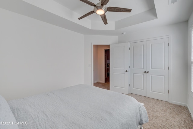 bedroom featuring carpet, a closet, a raised ceiling, a ceiling fan, and baseboards