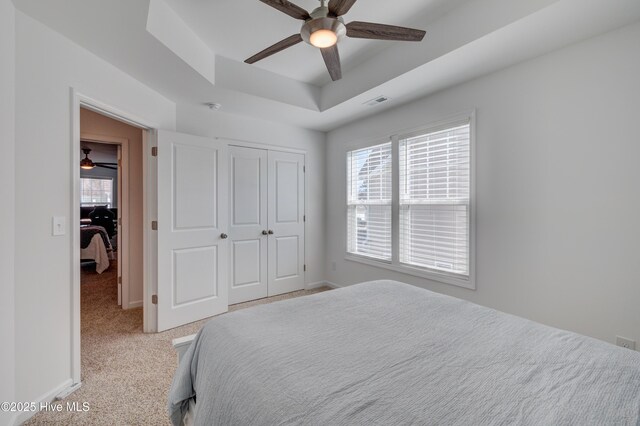 bedroom with a tray ceiling, a closet, light colored carpet, and baseboards