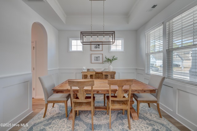 dining space with arched walkways, wood finished floors, a raised ceiling, and visible vents