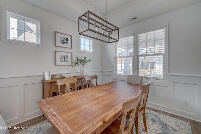 dining space featuring visible vents, a wainscoted wall, wood finished floors, a chandelier, and a decorative wall