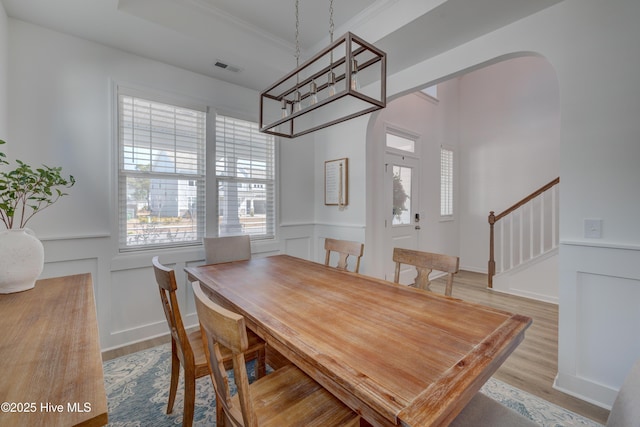 dining room featuring visible vents, arched walkways, stairway, wood finished floors, and a decorative wall