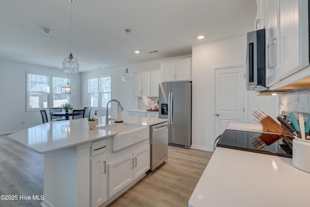 kitchen with stainless steel appliances, light countertops, white cabinets, a sink, and light wood-type flooring