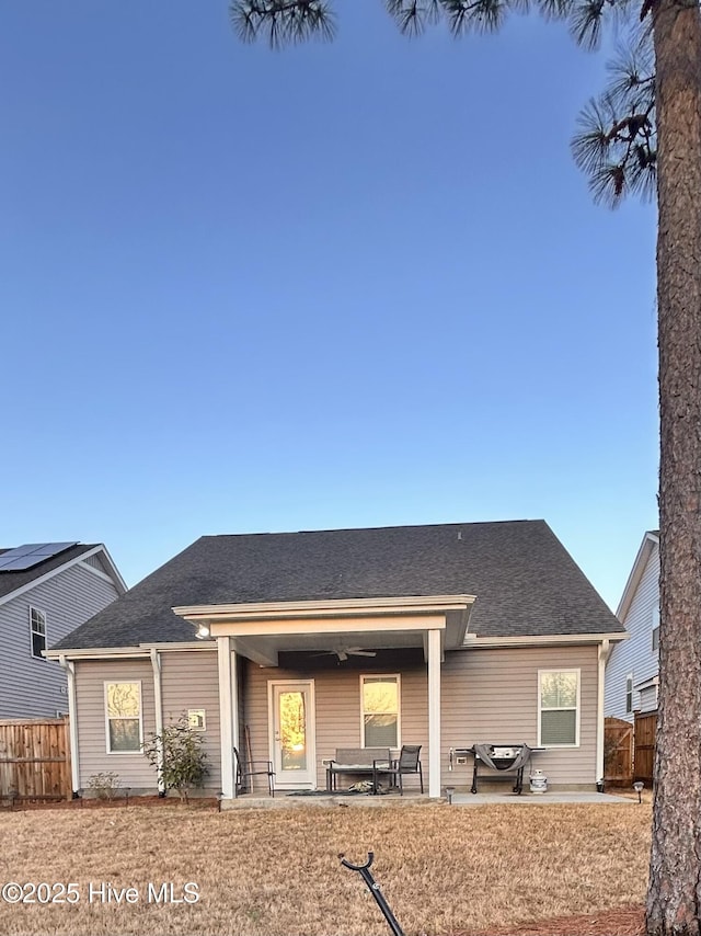 rear view of house featuring roof with shingles, fence, and a patio