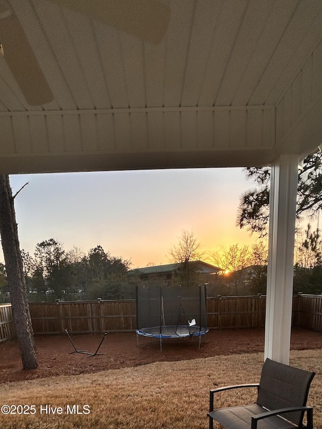 yard at dusk featuring a trampoline and fence