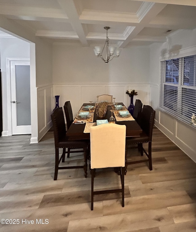 dining space with light wood-type flooring, an inviting chandelier, beam ceiling, and a wainscoted wall