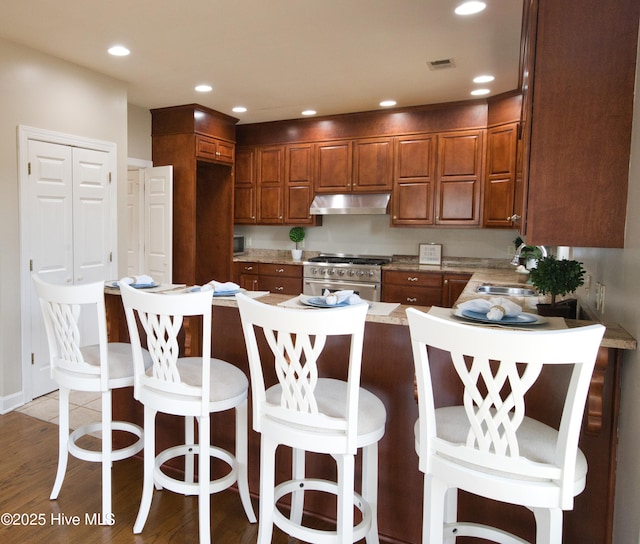 155 Abbington Pl SW, Ocean Isle Beach, NC 28469 - kitchen with high end stainless steel range oven, under cabinet range hood, a sink, wood finished floors, and brown cabinets