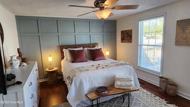 bedroom with visible vents, a decorative wall, dark wood-type flooring, a ceiling fan, and a textured ceiling