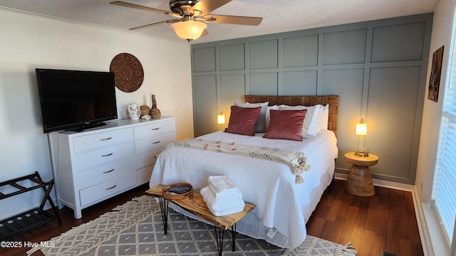 bedroom with a textured ceiling, dark wood-style flooring, a ceiling fan, and a decorative wall