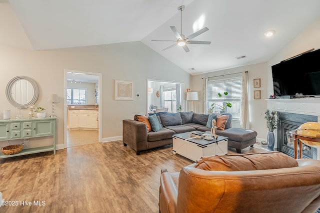 living room with lofted ceiling, visible vents, a ceiling fan, light wood finished floors, and a glass covered fireplace