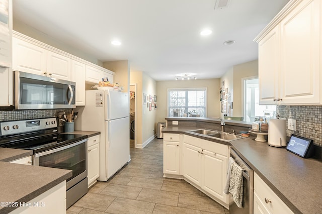 kitchen with appliances with stainless steel finishes, dark countertops, white cabinetry, and a sink