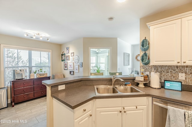 kitchen with dark countertops, white cabinets, a sink, dishwasher, and a peninsula