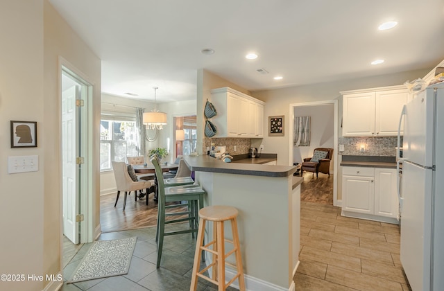 kitchen with freestanding refrigerator, white cabinetry, a peninsula, and a kitchen breakfast bar