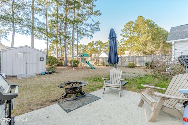 view of patio with a storage shed, an outdoor fire pit, a fenced backyard, an outbuilding, and a playground