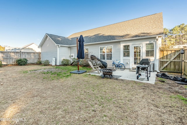 rear view of house with a fire pit, fence, roof with shingles, a lawn, and a patio area