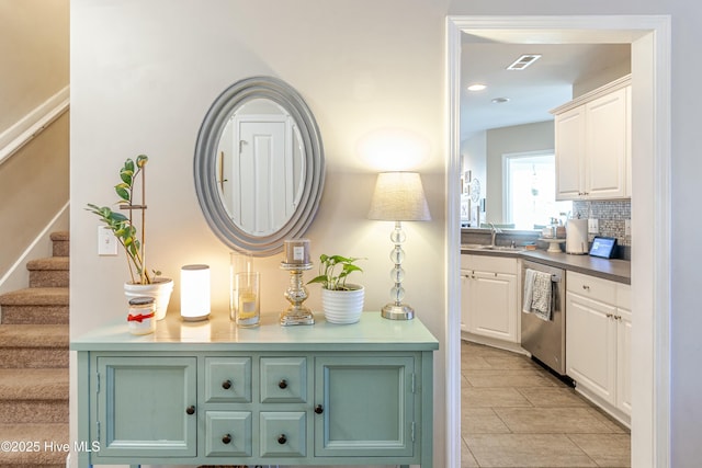 interior space featuring visible vents, decorative backsplash, a sink, dishwasher, and stairs