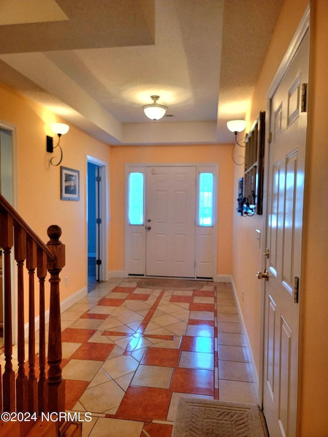 foyer featuring a raised ceiling, stairway, baseboards, and light tile patterned floors