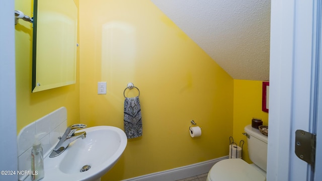 bathroom featuring a textured ceiling, toilet, a sink, baseboards, and vaulted ceiling