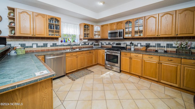 kitchen featuring open shelves, dark countertops, glass insert cabinets, appliances with stainless steel finishes, and a sink