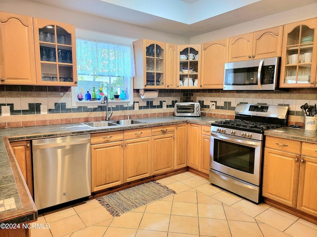 kitchen featuring light brown cabinets, stainless steel appliances, a sink, and glass insert cabinets