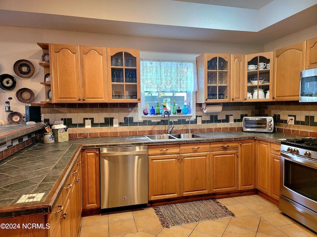 kitchen with open shelves, dark countertops, appliances with stainless steel finishes, glass insert cabinets, and a sink