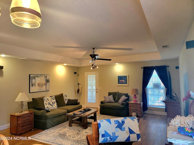 living room featuring baseboards, visible vents, a raised ceiling, dark wood-type flooring, and a textured ceiling