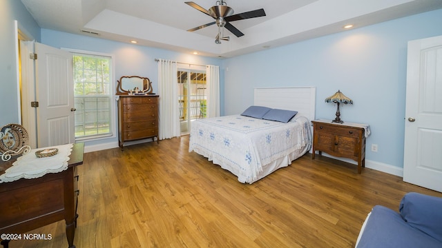 bedroom with baseboards, a raised ceiling, wood finished floors, and recessed lighting